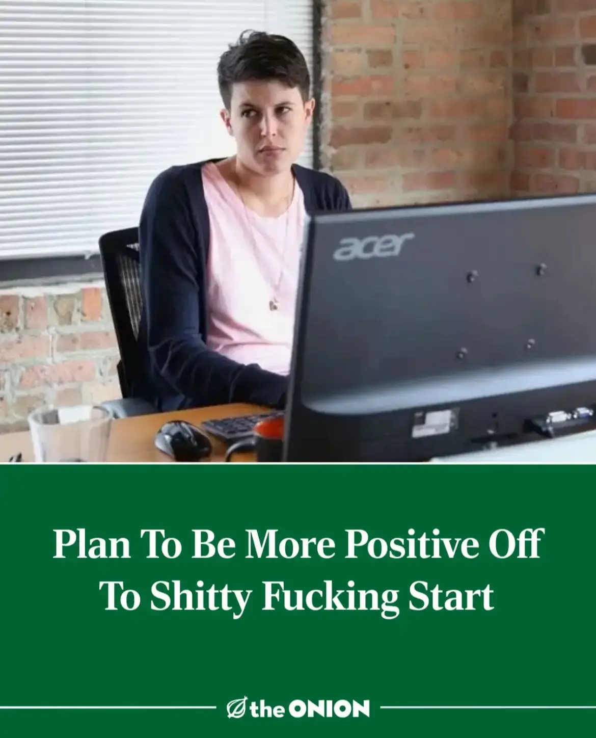 A person with short dark hair sits at a desk in front of an Acer computer monitor, looking frustrated or annoyed. The image…