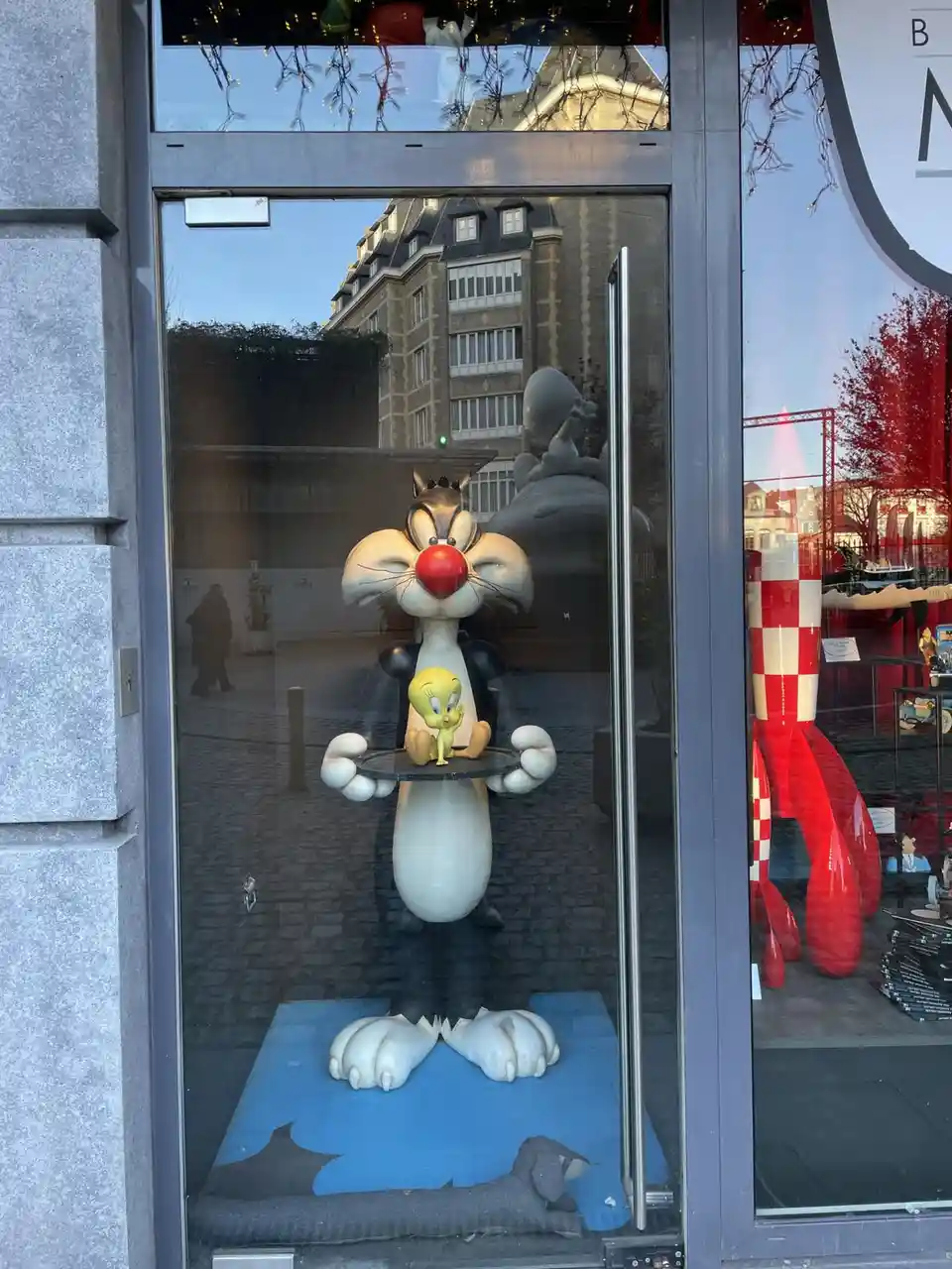 A large statue of the cartoon cat Sylvester is displayed in a store window, holding a small yellow bird, Tweety Bird, on a…