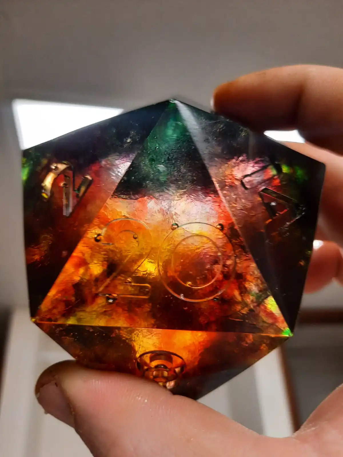 A hand holds a translucent, iridescent 20-sided die with metallic numbers, showing the number 20 prominently on its face…
