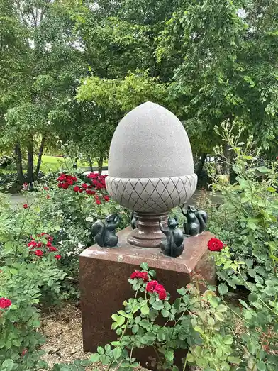 A garden sculpture features a large stone acorn atop a pedestal, surrounded by four bronze squirrel statues in various…