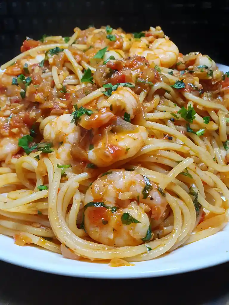 A close-up photo of a plate of spaghetti with shrimp in a tomato-based sauce, garnished with chopped parsley. The background…