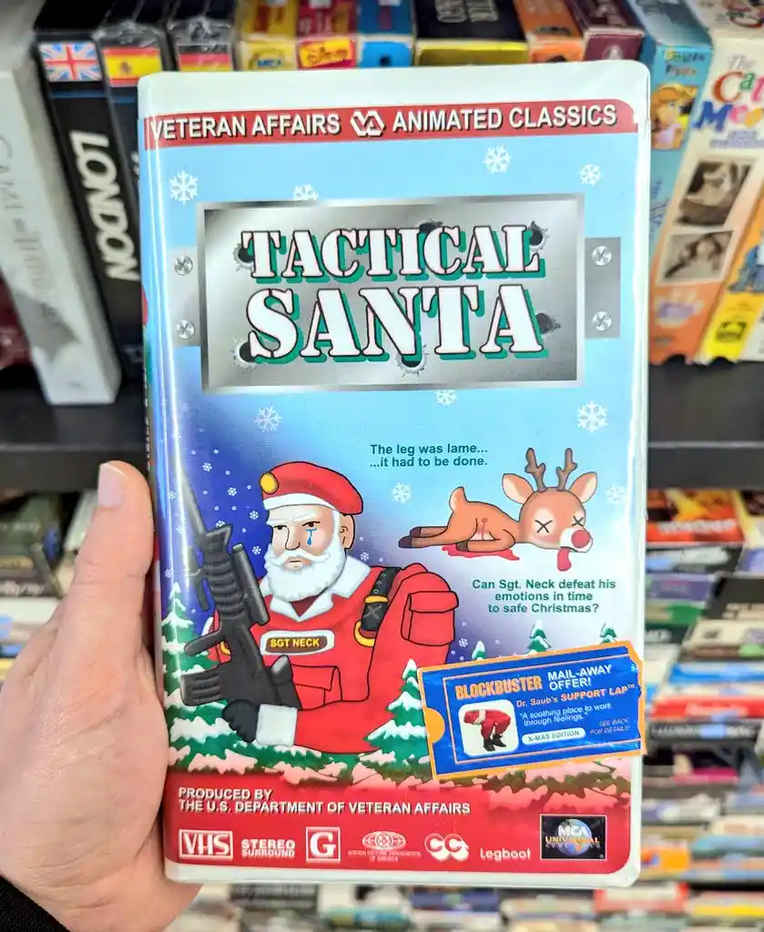 A hand holds a VHS tape labeled 'Tactical Santa,' depicting a grim, militarized Santa Claus holding a rifle, with a dead…