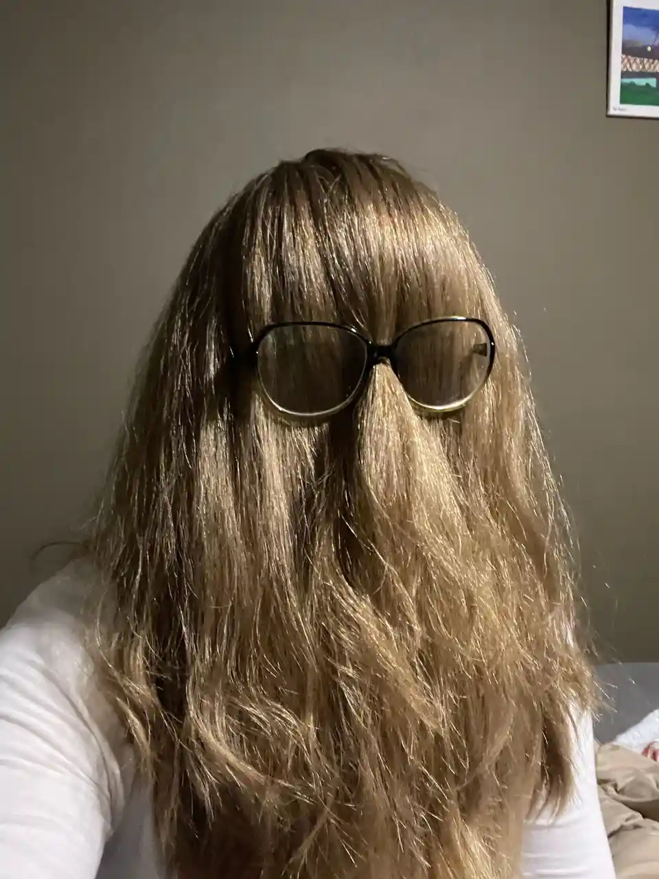 A person with long, wavy, light brown hair is shown from the shoulders up, wearing dark sunglasses that sit atop their head…