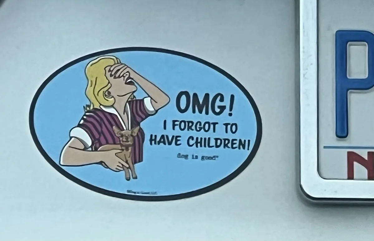 A blue oval sticker on a car shows a cartoon woman with blonde hair holding a small dog, one hand on her forehead in shock…