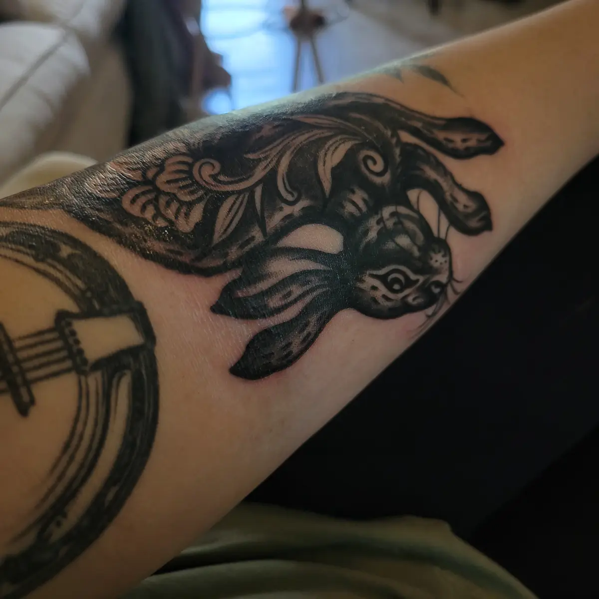 A close-up photo shows a person's forearm with two black-and-gray tattoos: a detailed, stylized rabbit with long ears and…
