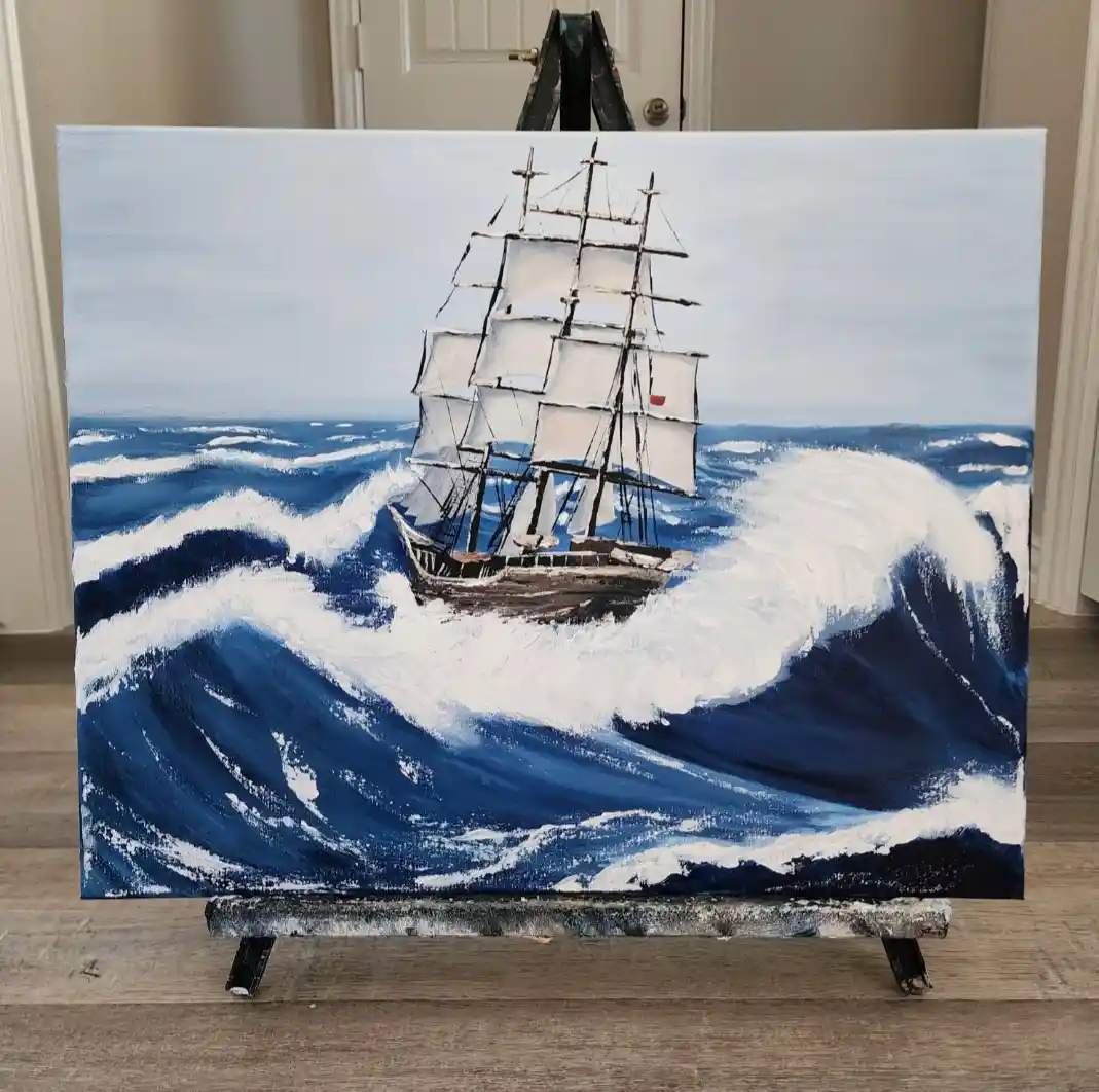 A painting of a tall ship with full sails navigating turbulent, crashing ocean waves is displayed on an easel indoors. The…
