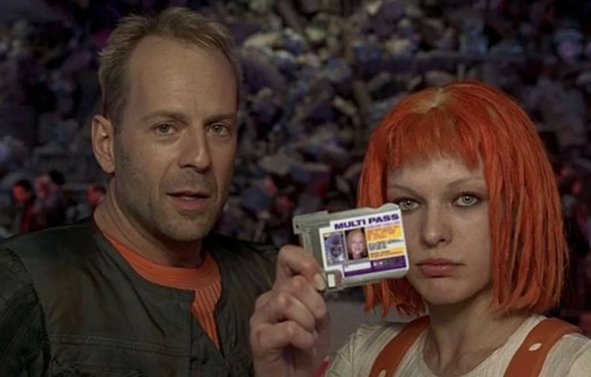 A man and a woman stand in a crowded arena, the woman holding up a plastic card labeled 'MULTI PASS' with two photos on it…
