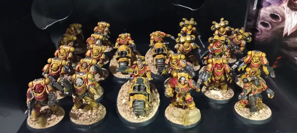 A collection of intricately painted yellow and red armored miniature figures, some on motorcycles, arranged on textured…