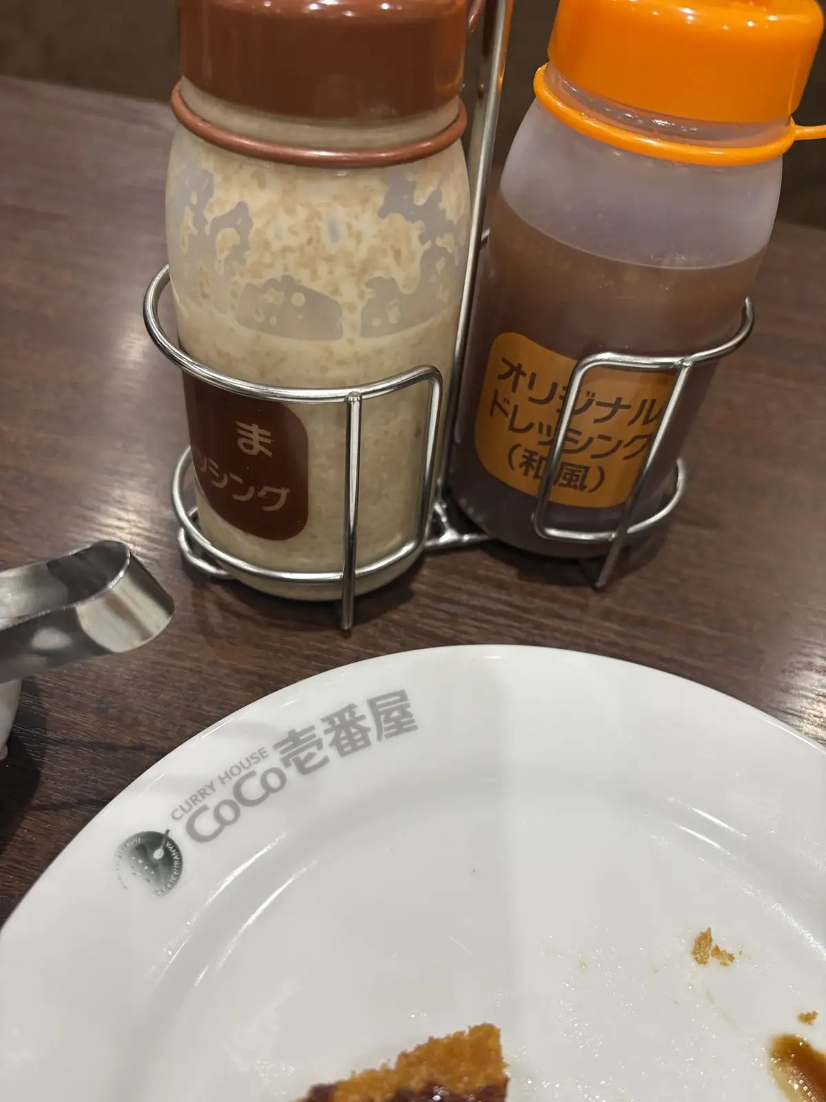 A close-up photo shows two condiment bottles in a metal holder on a wooden table, next to an empty white plate with 'CURRY…