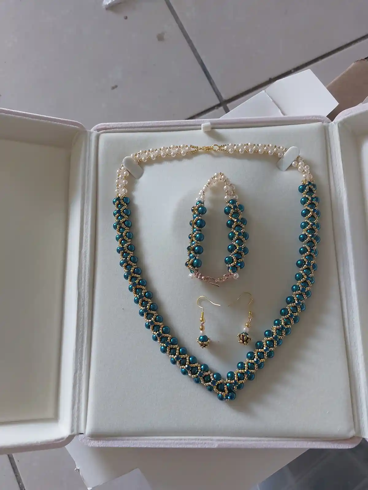 A handmade jewelry set featuring a necklace, a pair of hoop earrings, and a pair of drop earrings, all crafted with blue…
