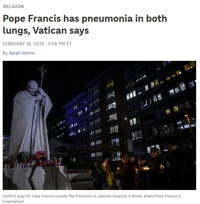 A nighttime photo shows a large white statue of Pope Francis holding a cross, with people holding candles praying nearby…