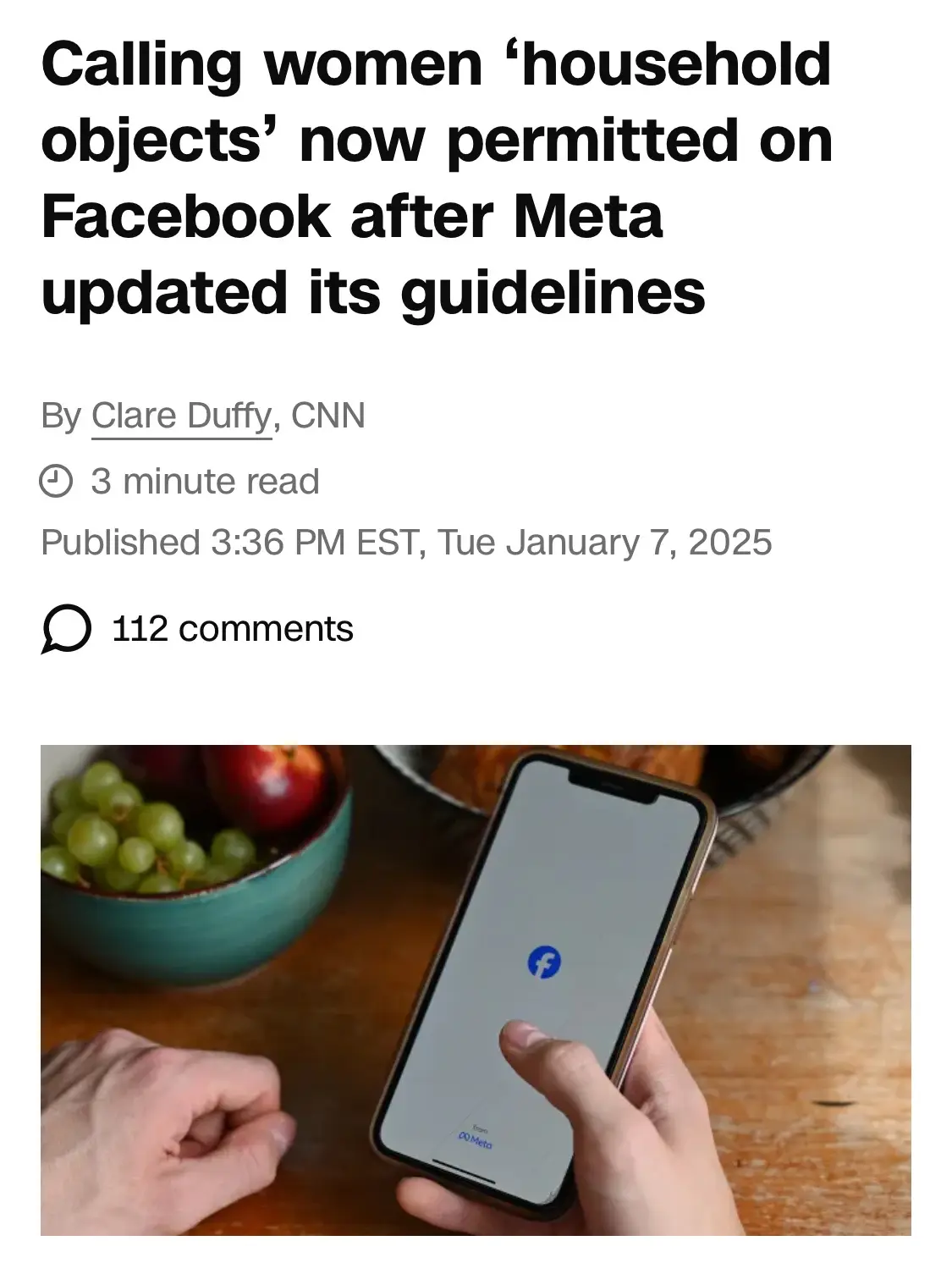 An image of a smartphone displaying the Facebook app logo, held by a hand over a wooden table with a bowl of fruit nearby…