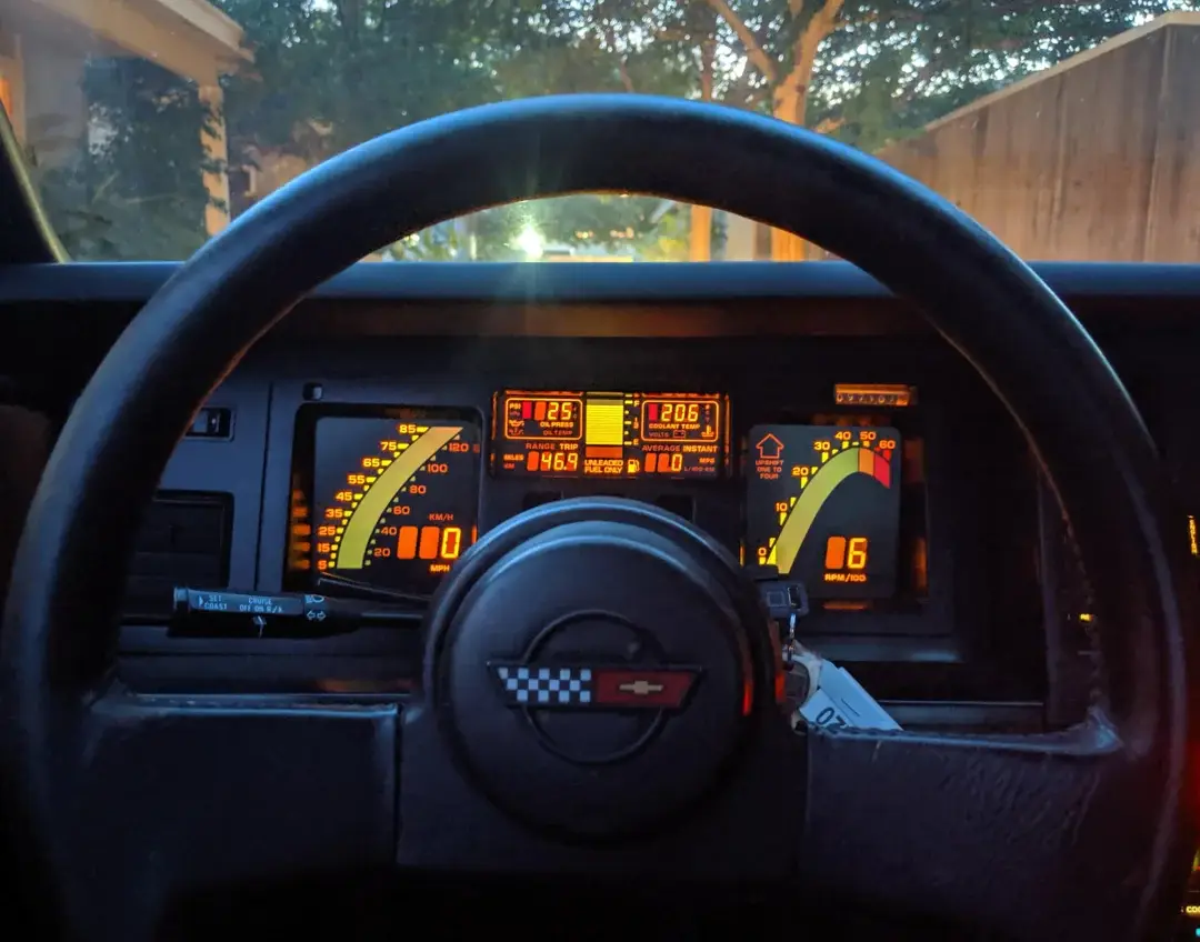 A close-up shot of a car's dashboard from the driver's perspective, showing an illuminated instrument cluster with orange…