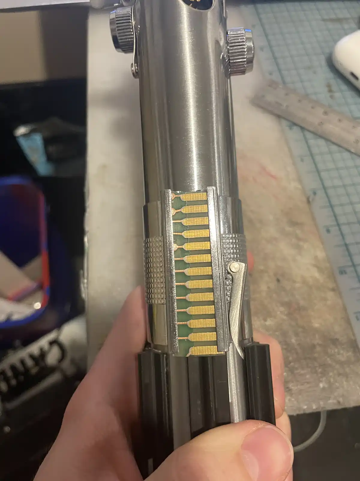 A close-up photo shows a person's hand holding a metallic lightsaber hilt with its internal circuit board exposed, revealing…