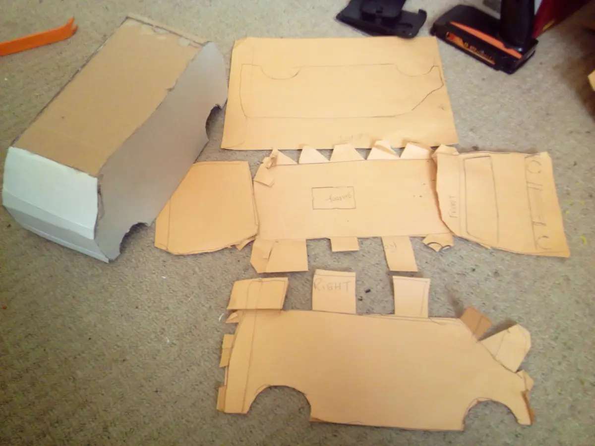 A collection of cardboard car body panels laid out on a carpeted floor, with handwritten labels like 'left', 'front'…