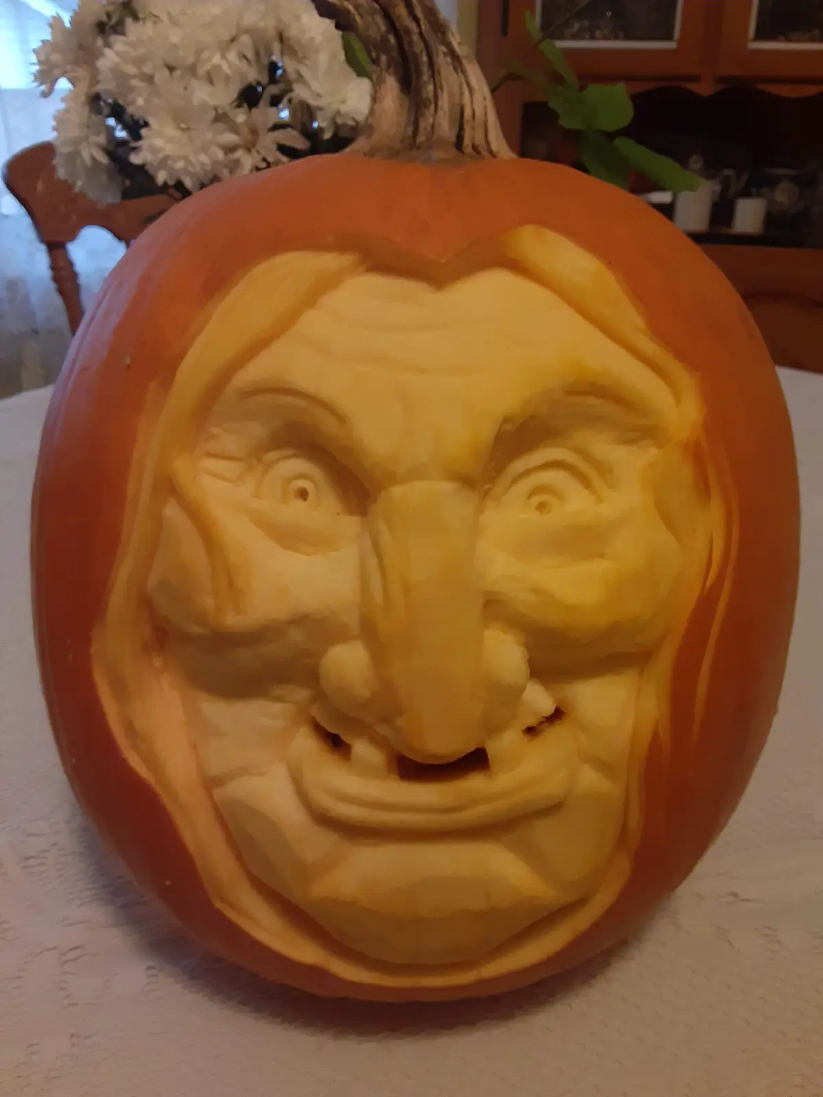 A close-up of a meticulously carved pumpkin with a detailed, realistic human face featuring a long, prominent nose, wide…