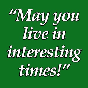 A solid green background with white text in a stylized font that reads 'May you live in interesting times!' The text is…