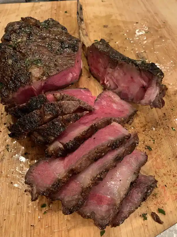 A close-up photo shows a sliced, medium-rare steak on a wooden cutting board, with a seared crust and pink interior…