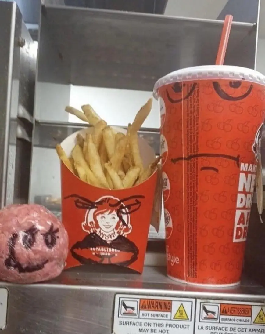 A close-up photo shows a raw, pink meatball with a crudely drawn smiling face on it, sitting next to a Wendy's french fry…