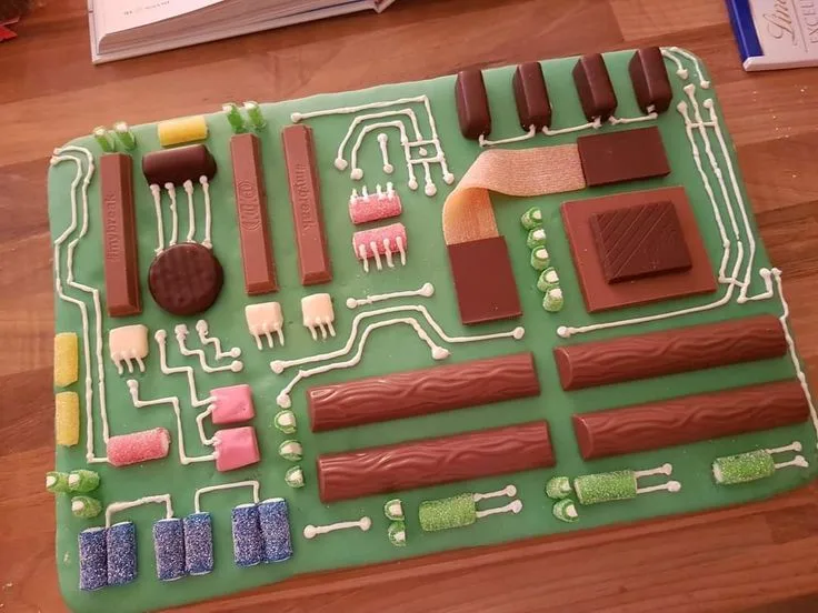 a rectangular cake with a green fondant base is decorated to resemble a computer circuit board, featuring white icing lines…
