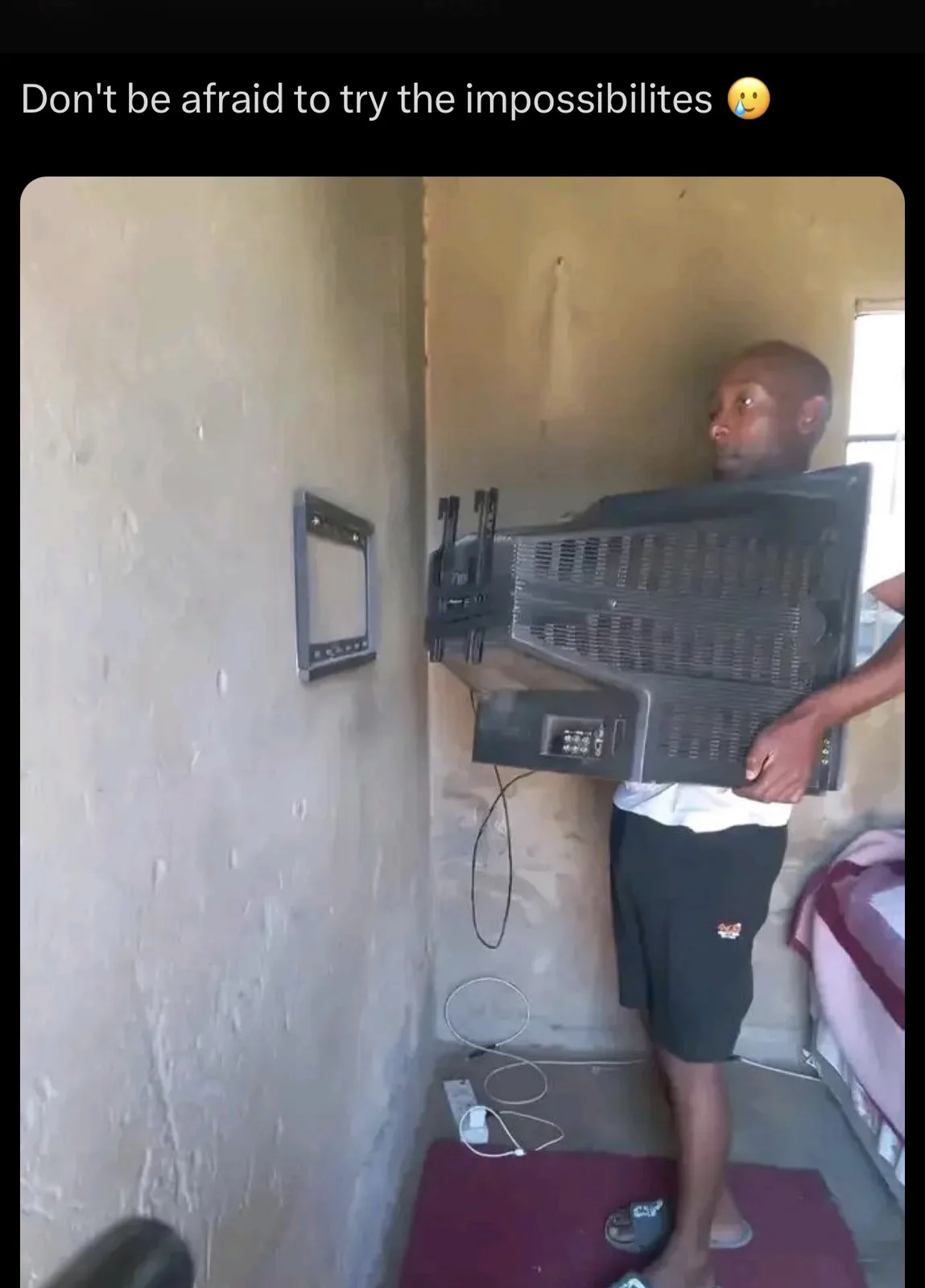 A man is holding a large, bulky CRT television with its back facing the viewer, attempting to mount it on a wall bracket…