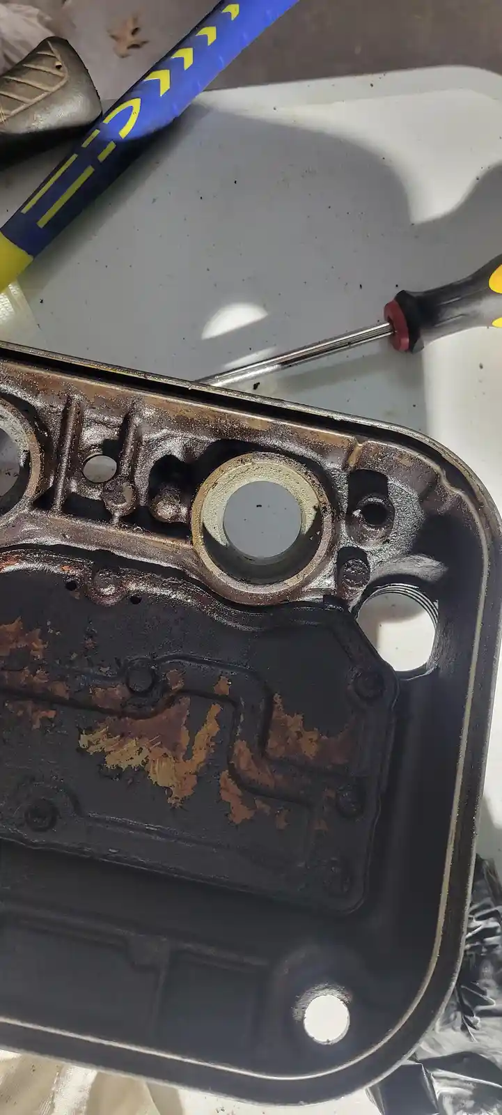 A close-up photo shows a heavily rusted and dirty car engine part, likely a valve cover or oil pan, with visible corrosion…