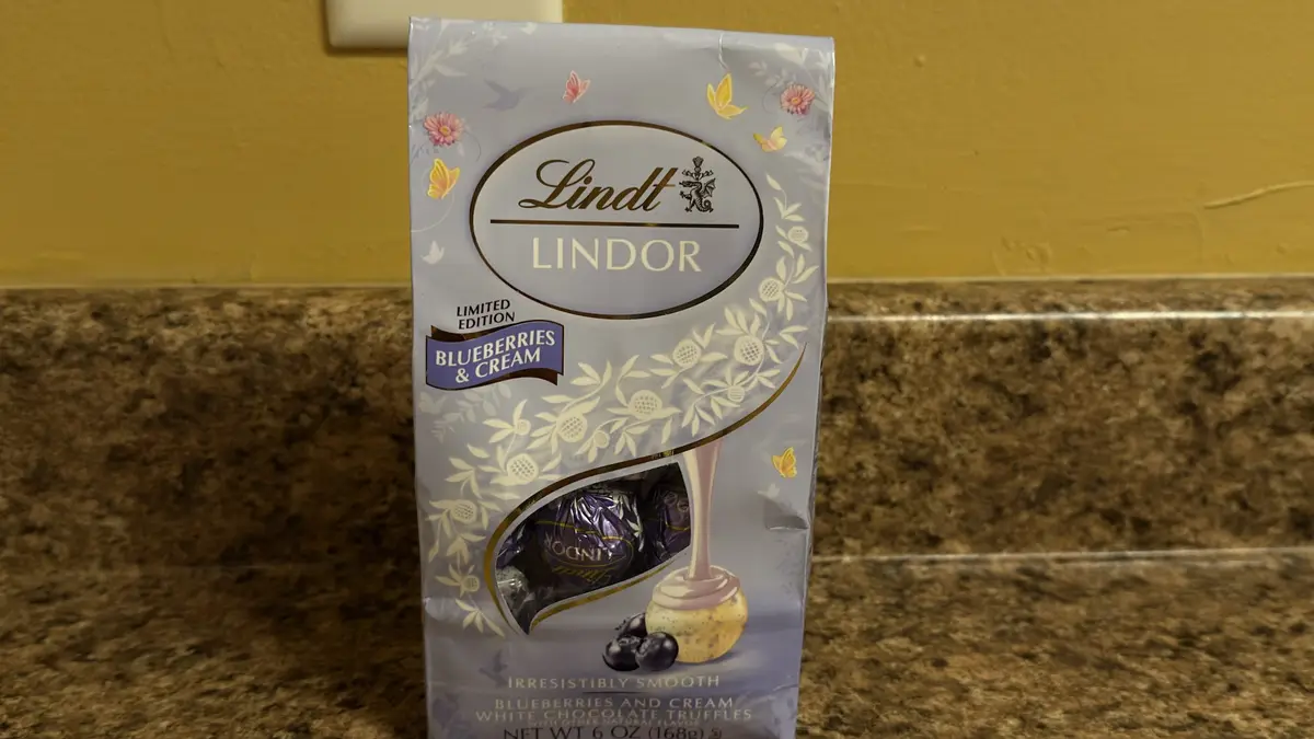 A bag of Lindt LINDOR limited edition blueberries & cream white chocolate truffles sits on a brown speckled countertop…