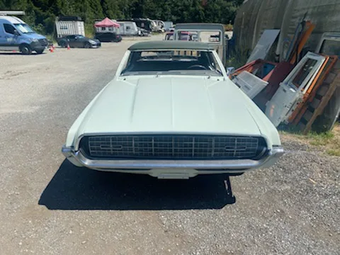 a light green classic car is shown from the front, missing its hood and featuring a large, gaping hole where the engine…