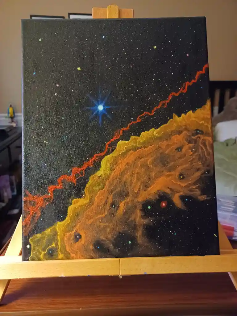 A hand-painted canvas on an easel depicts a cosmic scene with a starry black sky, a bright blue star, and a wavy orange…