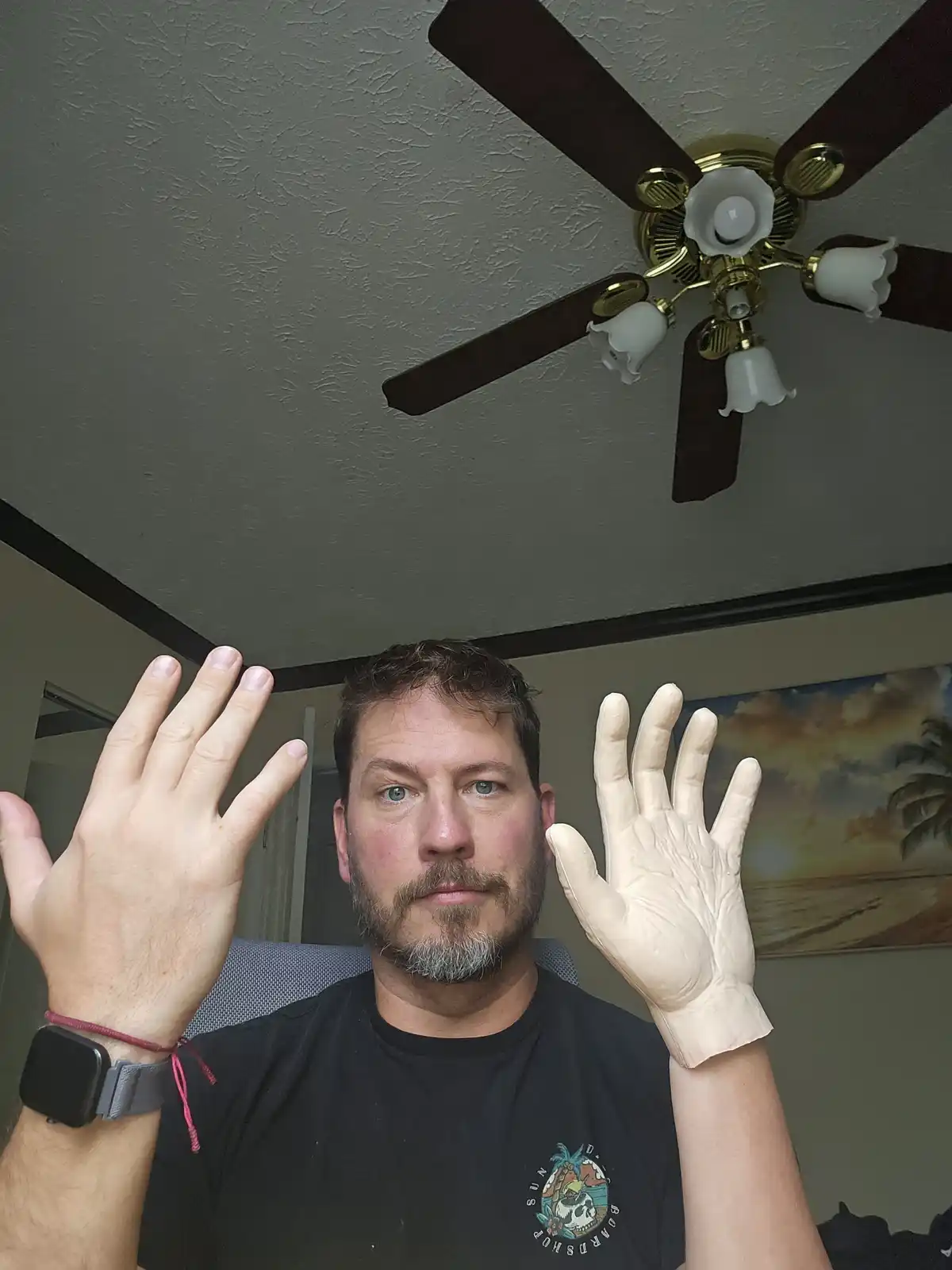 A man with a beard and blue eyes looks at the camera with both hands raised, showing five fingers on his bare right hand and…