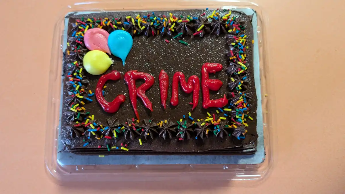 A rectangular chocolate cake in a clear plastic container, decorated with colorful sprinkles and piped frosting balloons…