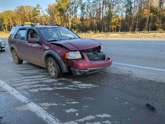 A maroon SUV is severely damaged at the front end, parked on a road with visible skid marks and debris. The overlaid text…