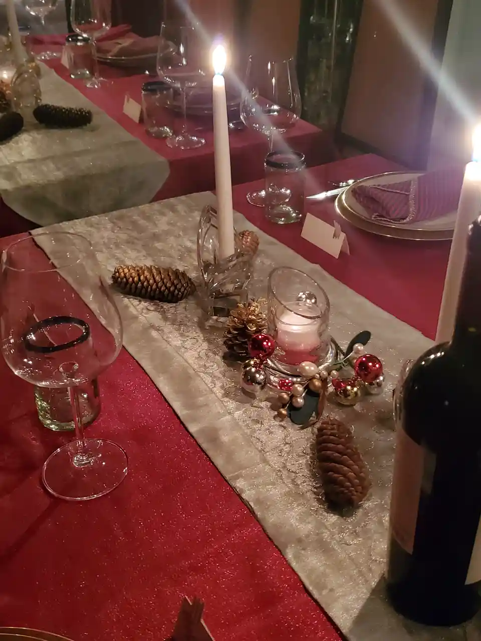 A festive holiday table setting with red glitter tablecloths, silver runners, pinecones, and lit candles, overlaid with the…