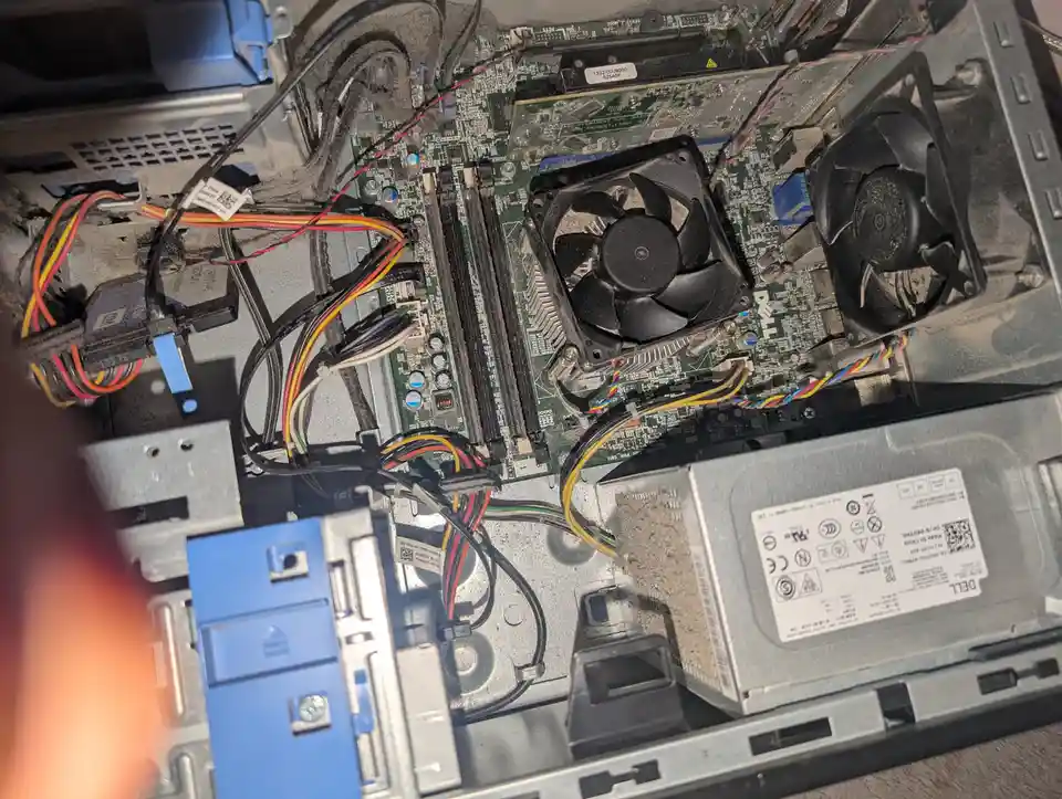 A dusty, disassembled Dell computer case interior showing a motherboard, two black CPU coolers with fans, tangled colorful…
