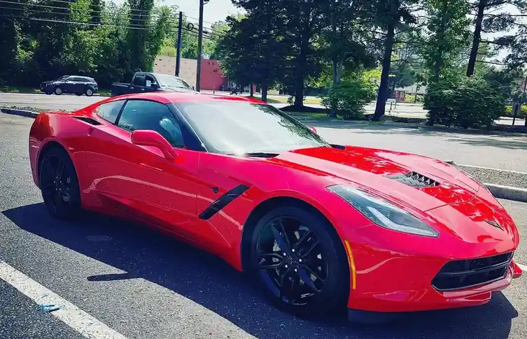 A shiny red Chevrolet Corvette sports car is parked in a sunny parking lot, its sleek body and black wheels reflecting the…