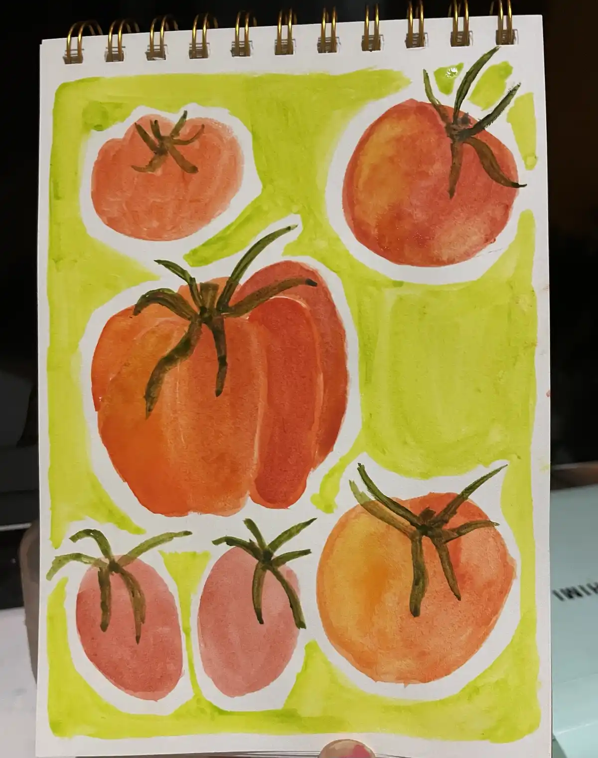 A watercolor drawing on a spiral-bound notebook page shows six tomatoes arranged in a grid, each in its own white oval…