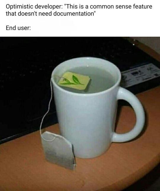 A white ceramic mug with a tea bag inside sits on a wooden surface next to a laptop. The tea bag's string hangs down, and…