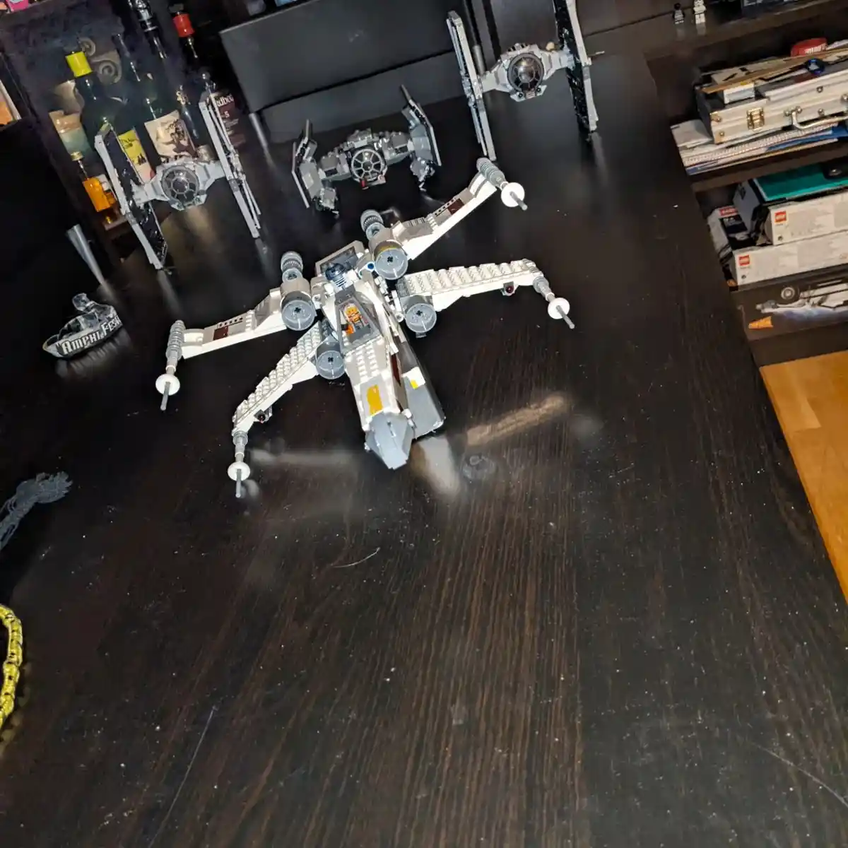 A photo shows a completed LEGO X-wing starfighter model on a dark wooden table, with several other LEGO starfighters and…