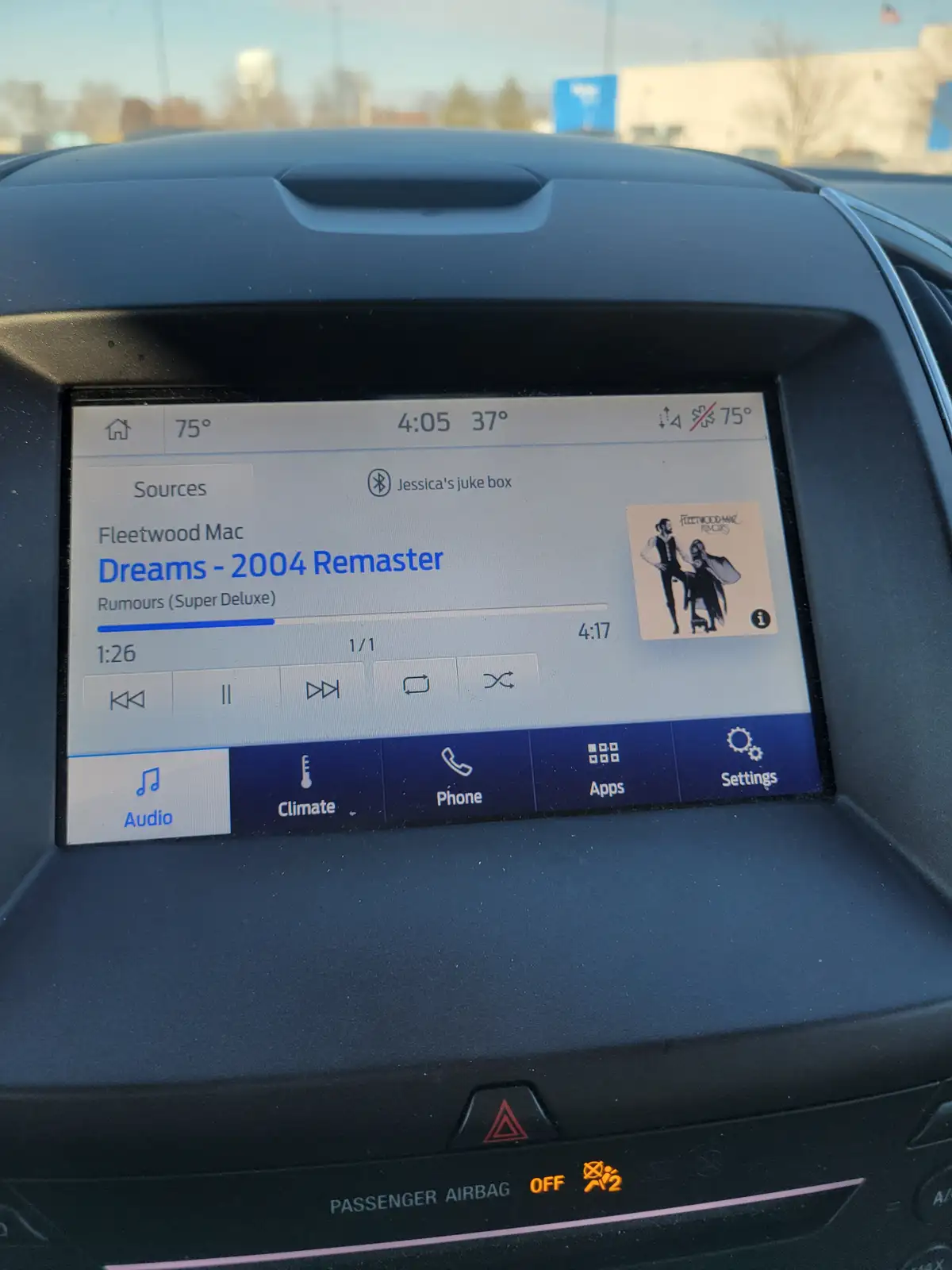 A car's infotainment screen shows Fleetwood Mac's 'Dreams - 2004 Remaster' playing from a source labeled 'Jessica's juke…