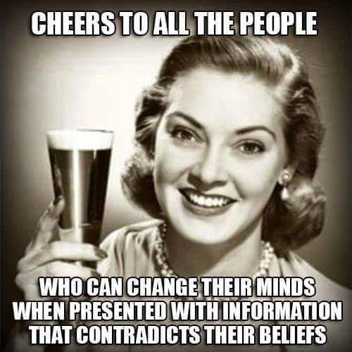 A black-and-white photo of a smiling woman from the 1940s or 1950s holding a glass of beer or ale. She has styled hair…