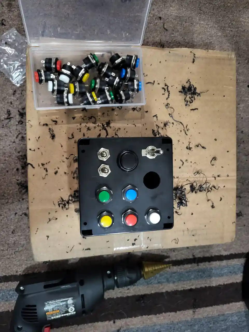 An overhead shot shows a black arcade button panel with six colored buttons (green, blue, yellow, red, white, and one black)…
