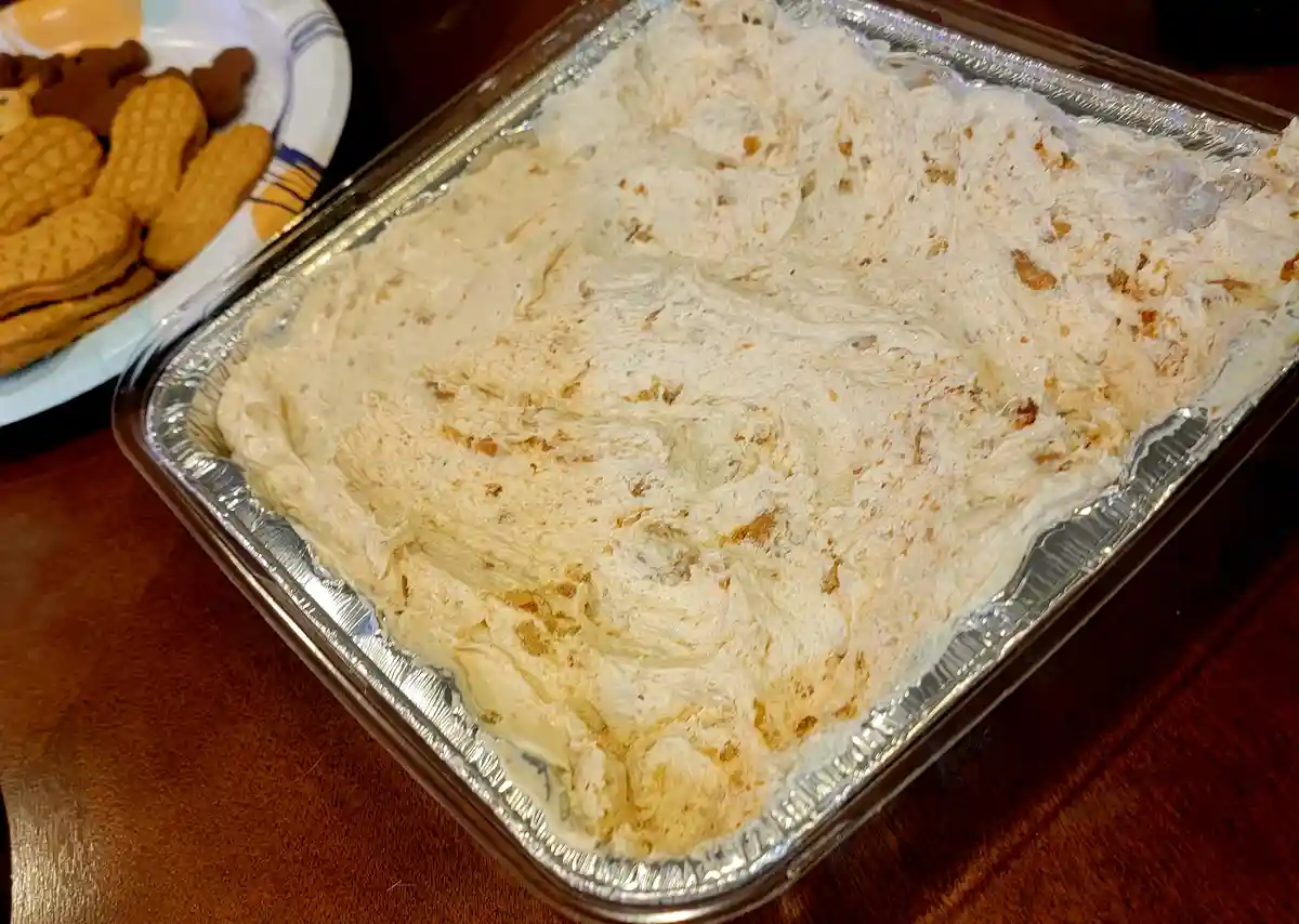 A close-up photo shows a rectangular aluminum baking pan filled with a creamy, light-brown dessert dip, likely peanut butter…