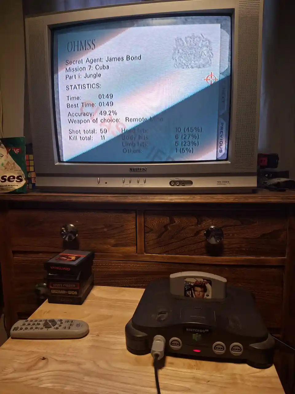 A Nintendo 64 console with an 'OHMSS' game cartridge inserted is shown on a wooden table, with a CRT television displaying…