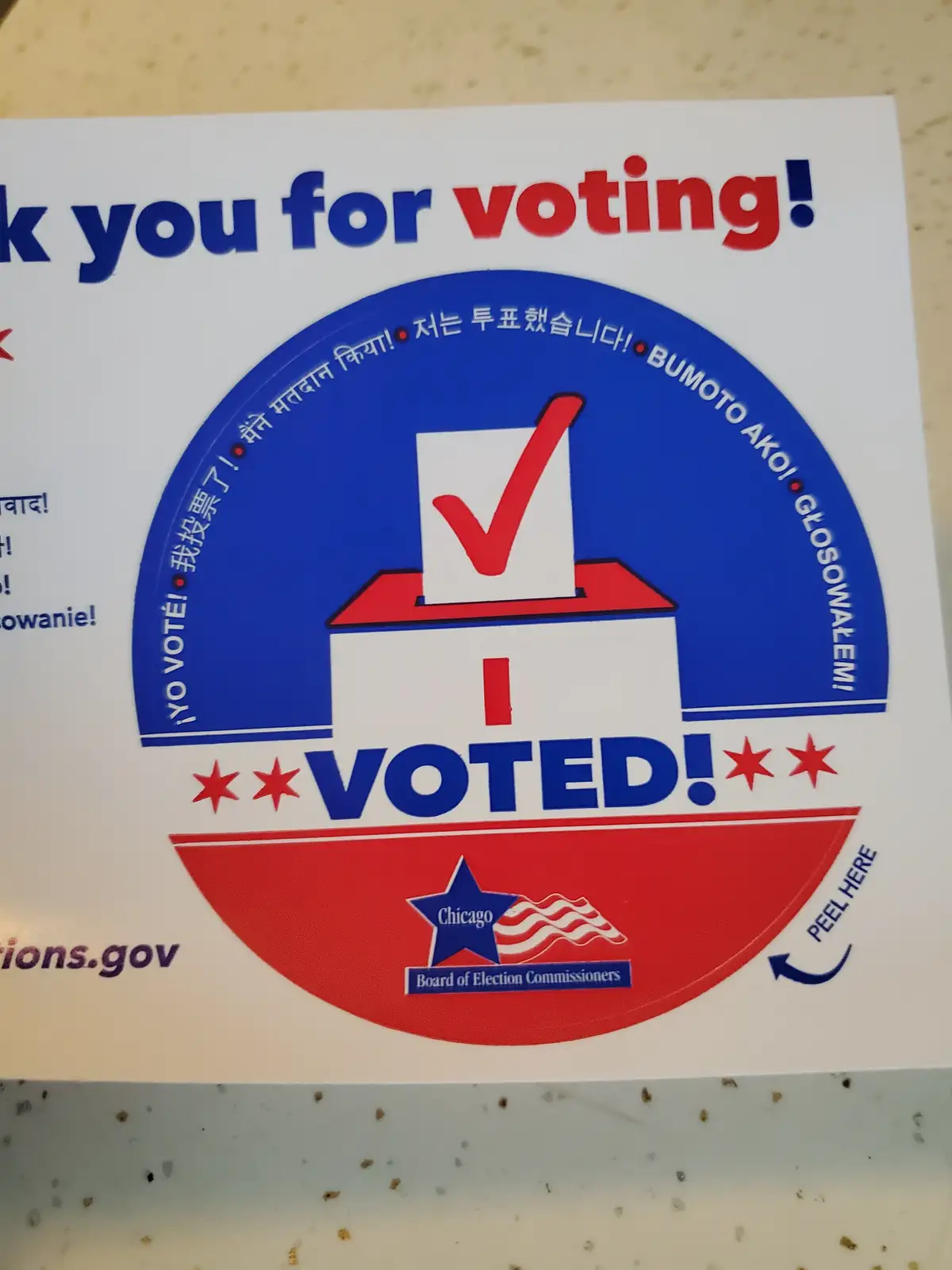 A close-up of a Chicago 'I VOTED!' sticker featuring a red checkmark in a ballot box, surrounded by multilingual phrases…
