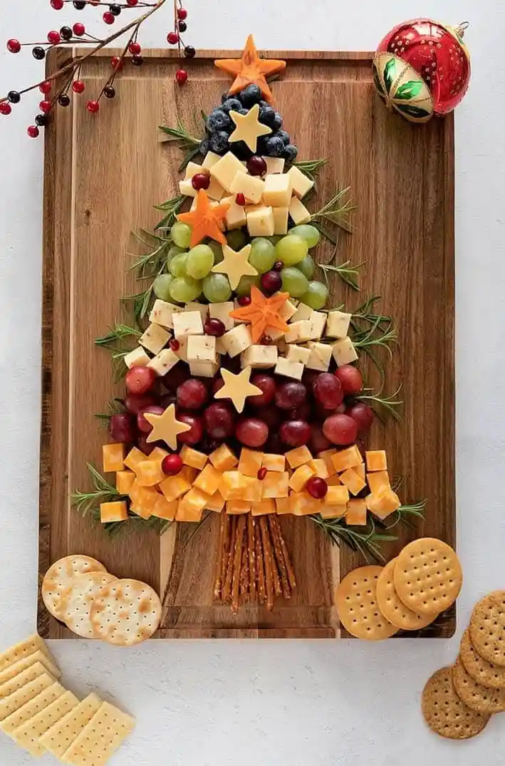 a festive christmas tree-shaped charcuterie board made from layered cheese cubes, green and red grapes, and star-shaped…
