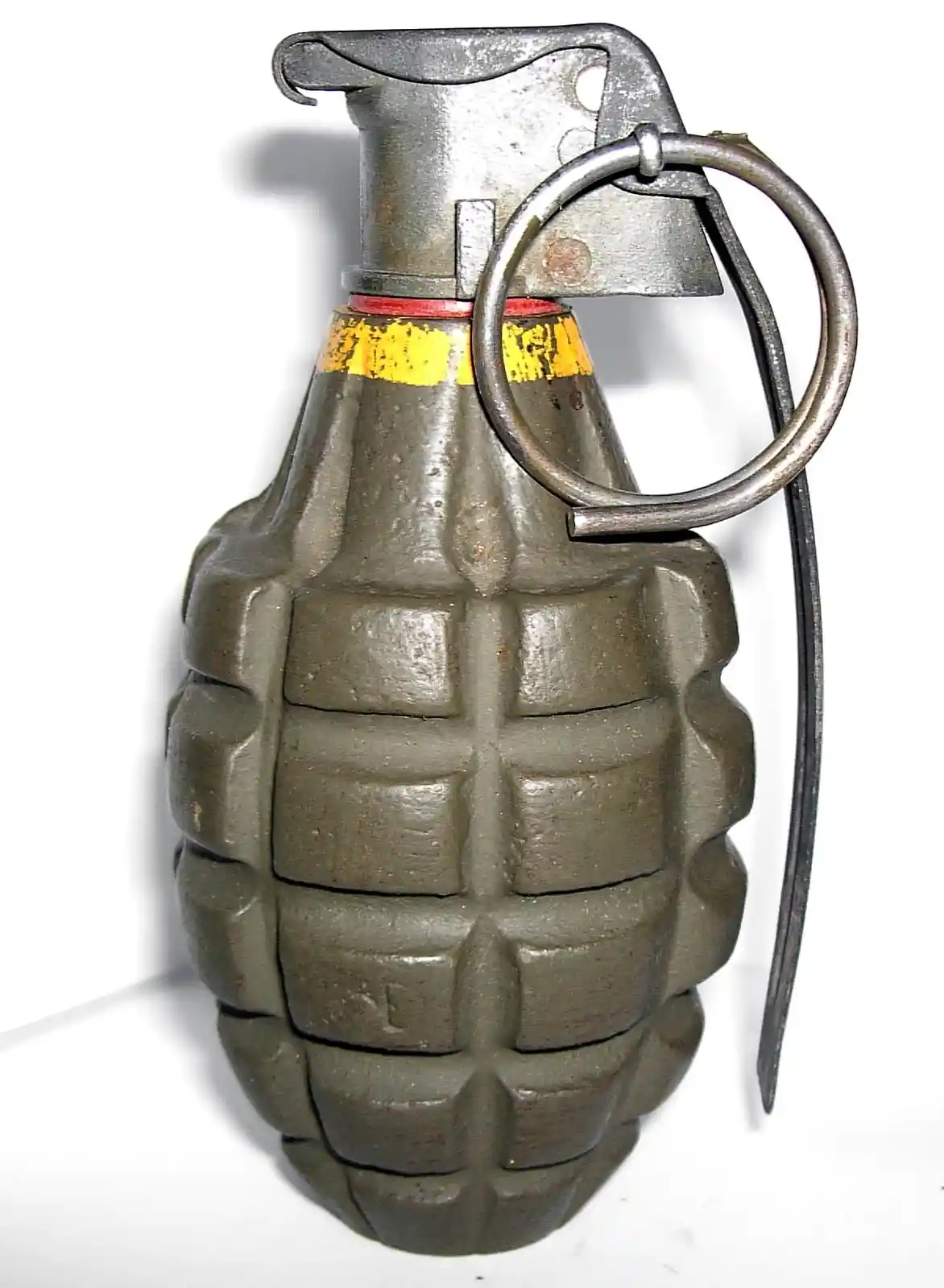 A close-up photograph of a real hand grenade with a metal fuze, safety pin, and pull ring against a white background. The…