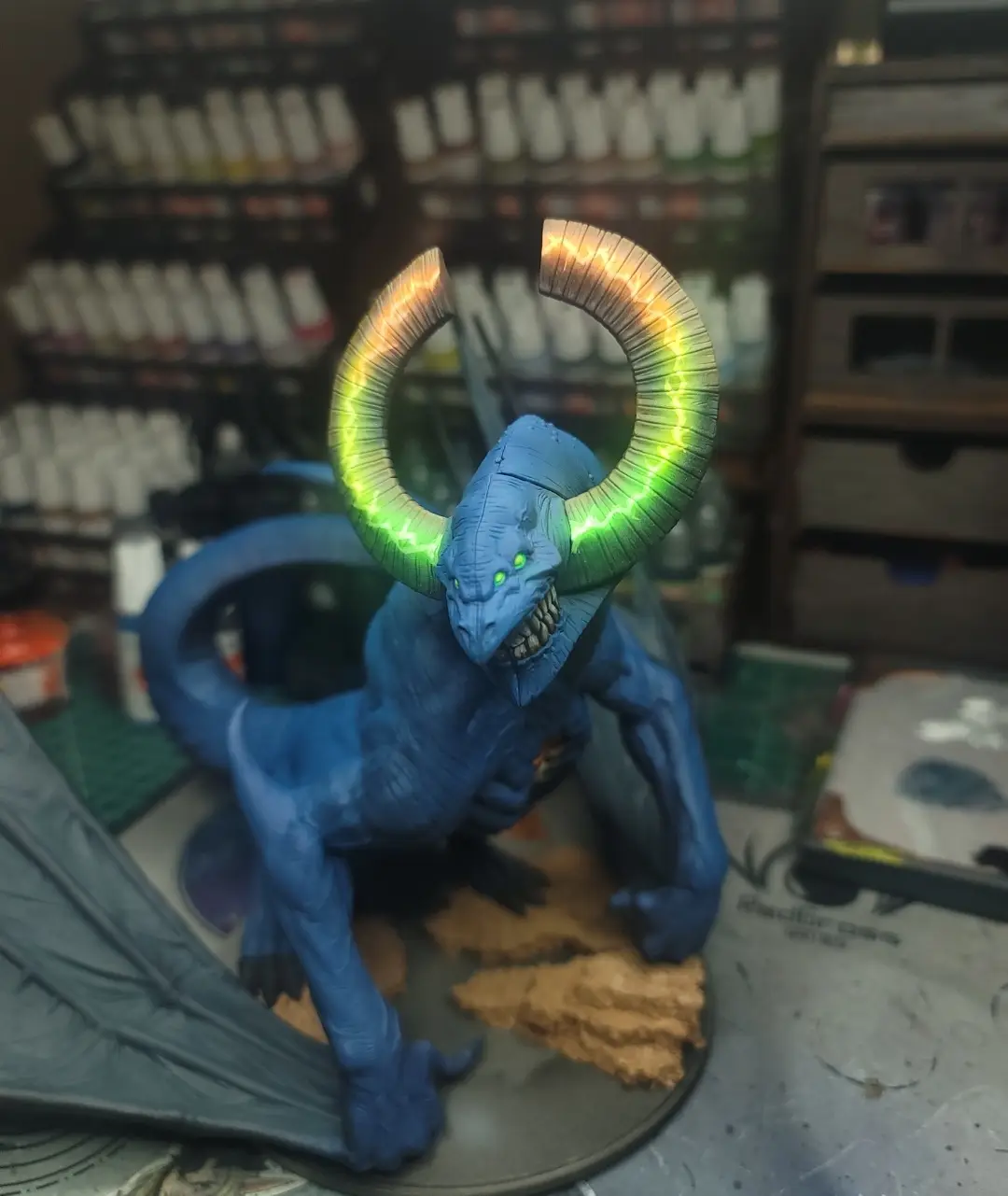 A blue, muscular, horned monster figurine with glowing green eyes and large, curved horns that emit a green and yellow…