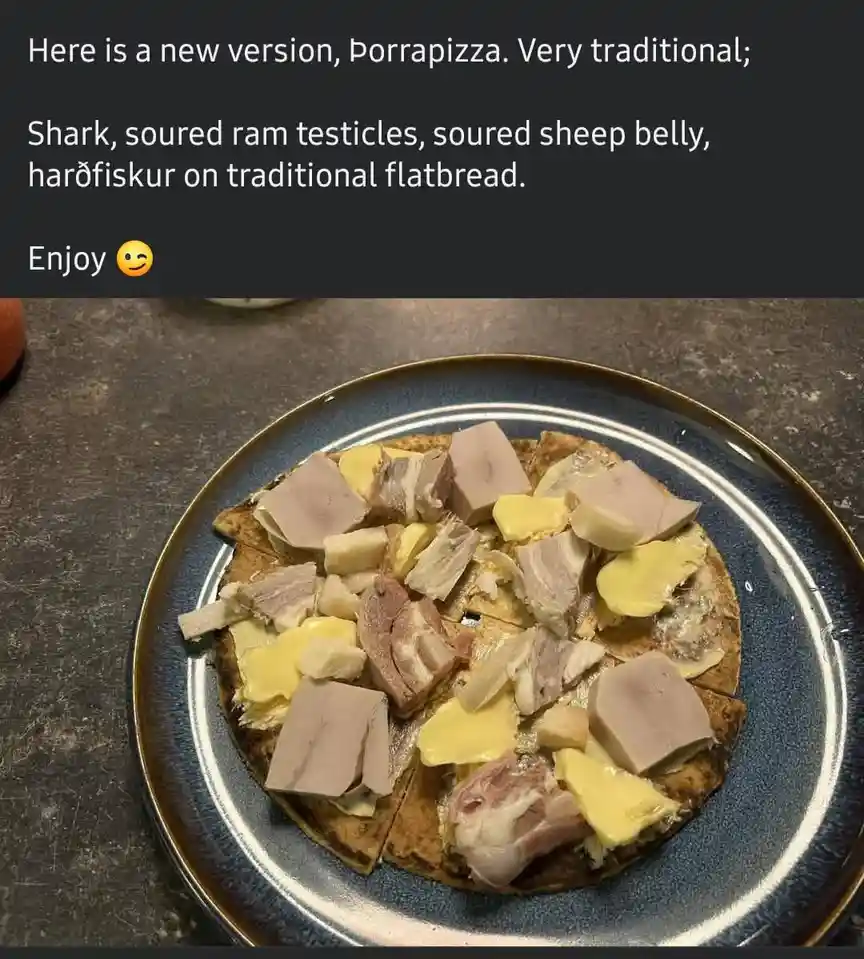 A round flatbread pizza on a blue plate is topped with chunks of pale meat, yellow cheese, and other unidentifiable…