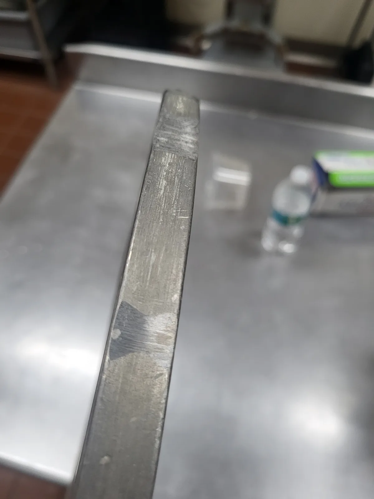 A close-up photo shows the heavily scratched and worn edge of a metal knife resting on a stainless steel countertop, with a…