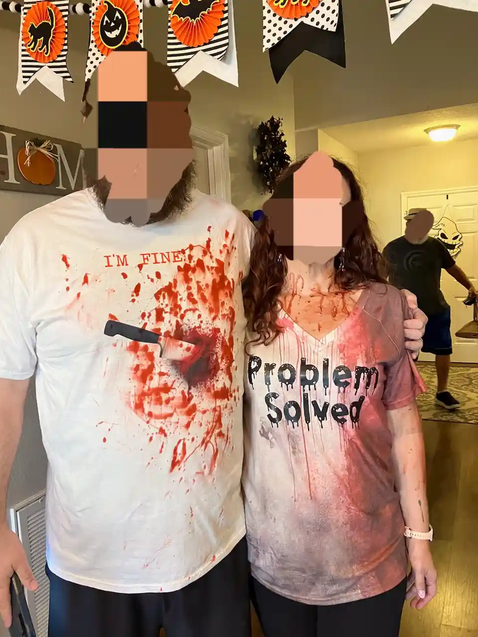 Two people in a Halloween setting, their faces blurred, stand side by side with fake blood splattered on their clothes. The…